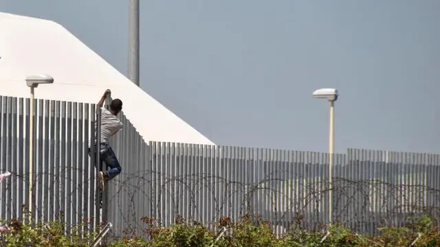 Un immigrato del Cara scavalca la protezione del centro di immigrazione di Bari, 3 luglio 2013 . La polizia sta interrogando gli ospiti e il personale in servizio al Cara di Bari per ricostruire le cause della rissa che si è scatenata la scorsa notte nel centro di accoglienza e individuare le persone chi vi hanno preso parte. Le indagini, condotte dalla squadra mobile, sono coordinate dal sostituto procuratore della Repubblica presso il Tribunale di Bari Renato Nitti. L'esame esterno del corpo del giovane ucciso è stato eseguito dal medico legale Biagio Solarino al quale nei prossimi giorni verrà affidata l'autopsia.ANSA/LUCA TURI