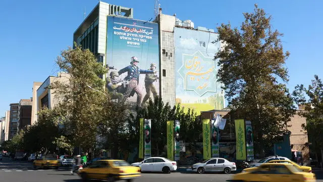 epaselect epa11705016 Iranians drive past an anti-US billboard carrying a sentence reading in Persian 'US is the big devil' hanged on a wall in Tehran, Iran, 06 November 2024. Tension between Iran and US is going as Donald Trump elected as the new US president. EPA/ABEDIN TAHERKENAREH