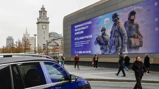 epa11652677 People walk past an electronic screen showing an advertisement calling for military conscription with the image of Russian soldiers near Kiyevsky railway station in Moscow, Russia, 10 October 2024. On 24 February 2022, Russian troops entered Ukrainian territory in what the Russian president declared a special military operation, starting an armed conflict. EPA/YURI KOCHETKOV