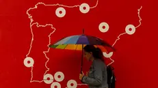 epa11690549 A woman holds an umbrella while walking in front of a poster with the map of Spain, in Malaga, Spain, 29 October 2024. The area is currently facing significant rainfall. EPA/JORGE ZAPATA