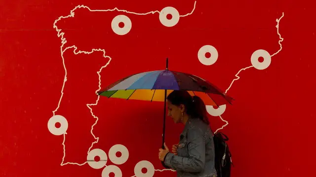 epa11690549 A woman holds an umbrella while walking in front of a poster with the map of Spain, in Malaga, Spain, 29 October 2024. The area is currently facing significant rainfall. EPA/JORGE ZAPATA