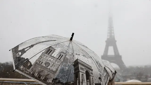 epa11733280 A person walks with an umbrella during snowfall near the Eiffel Tower in Paris, France, 21 November 2024. French National Weather and Climate Service Meteo-France issued an 'orange' warning in 32 departments from northern Brittany and Normandy to the Ile-de-France due to snowfall and freezing rain forecasted on 21 November. EPA/MOHAMMED BADRA