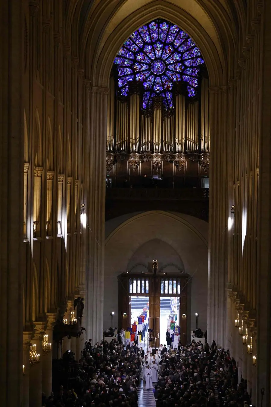 Members of the clergy and banner bearers walk towards the new main altar during its consecration, as part of the first mass for the public, at the Notre-Dame de Paris cathedral, in Paris, on December 8, 2024. Newly restored Notre Dame cathedral is set to hold its first service for the public on December 8, 2024 after a historic re-opening ceremony that saw firefighters, builders and artists celebrated for their work saving the 12th-century masterpiece. The beloved Paris monument nearly burned down in 2019, but has been renovated inside and fitted with a new roof and spire during a frenzied reconstruction effort since then. (Photo by Ludovic MARIN / AFP)