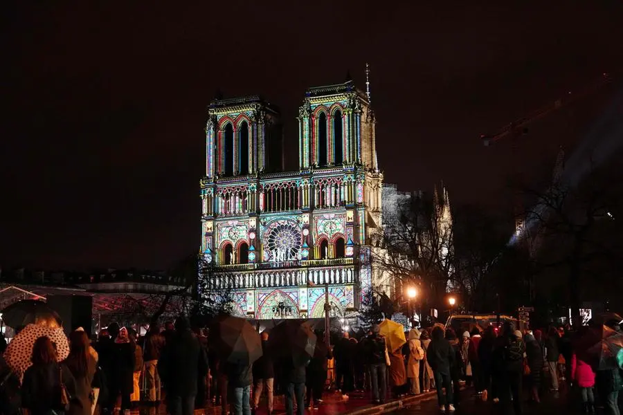 TOPSHOT - Crowds stand outside Notre-Dame Cathedral as it is illuminated during a ceremony to mark the re-opening of the landmark Cathedral, in central Paris, on December 7, 2024. Around 50 heads of state and government are expected in the French capital to attend the ceremony marking the rebuilding of the Gothic masterpiece five years after the 2019 fire which ravaged the world heritage landmark and toppled its spire. Some 250 companies and hundreds of experts were part of the five-year restoration project at a cost of hundreds of millions of euros. (Photo by Dimitar DILKOFF / AFP)