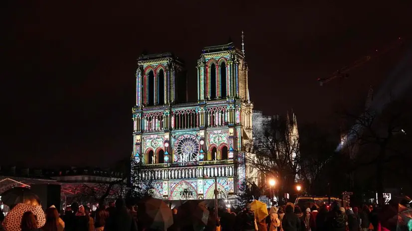 TOPSHOT - Crowds stand outside Notre-Dame Cathedral as it is illuminated during a ceremony to mark the re-opening of the landmark Cathedral, in central Paris, on December 7, 2024. Around 50 heads of state and government are expected in the French capital to attend the ceremony marking the rebuilding of the Gothic masterpiece five years after the 2019 fire which ravaged the world heritage landmark and toppled its spire. Some 250 companies and hundreds of experts were part of the five-year restoration project at a cost of hundreds of millions of euros. (Photo by Dimitar DILKOFF / AFP)