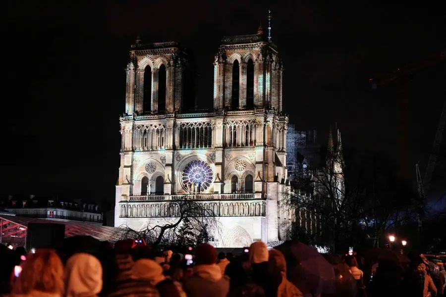 Crowds stand outside Notre-Dame Cathedral as it is illuminated during a ceremony to mark the re-opening of the landmark Cathedral, in central Paris, on December 7, 2024. Around 50 heads of state and government are expected in the French capital to attend the ceremony marking the rebuilding of the Gothic masterpiece five years after the 2019 fire which ravaged the world heritage landmark and toppled its spire. Some 250 companies and hundreds of experts were part of the five-year restoration project at a cost of hundreds of millions of euros. (Photo by Dimitar DILKOFF / AFP)