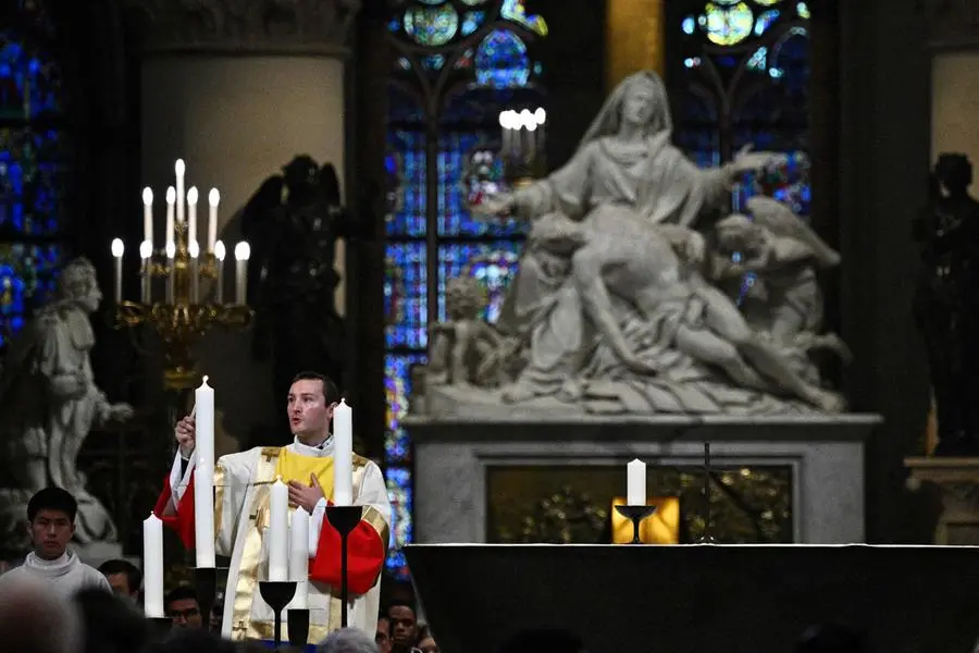 A prelate lights a candle during prayers lead by Archbishop of Paris for the consecration of the new altar, designed by French artist and designer Guillaume Bardet which replaces the old one that was destroyed in 2019, during a mass at the Notre-Dame de Paris cathedral, in Paris on December 8, 2024. Newly restored Notre Dame cathedral is set to hold its first service for the public on December 8, 2024 after a historic re-opening ceremony that saw firefighters, builders and artists celebrated for their work saving the 12th-century masterpiece. The beloved Paris monument nearly burned down in 2019, but has been renovated inside and fitted with a new roof and spire during a frenzied reconstruction effort since then. (Photo by JULIEN DE ROSA / AFP) / RESTRICTED TO EDITORIAL USE - MANDATORY MENTION OF THE ARTIST UPON PUBLICATION - TO ILLUSTRATE THE EVENT AS SPECIFIED IN THE CAPTION