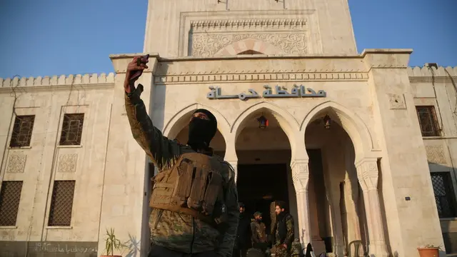 epa11760215 An opposition fighter takes a selfie in front of a Syrian government building after they entered the city of Hama, Syria, 06 December 2024. Syrian opposition forces, led by the Islamist militant group Hayat Tahrir al-Sham (HTS), launched an offensive on 27 November, triggering counterattacks by the Syrian regime forces as well as Russian and Syrian airstrikes on opposition-controlled areas. According to Hay'at Tahrir Al-Sham leader Abu Mohammad Al-Jolani, there will be 'no revenge' after opposition groups entered the strategically important Syrian city of Hama on 05 December. EPA/BILAL AL HAMMOUD