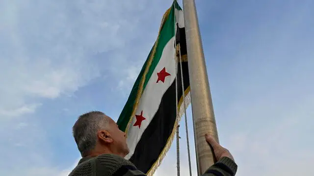 epa11769886 A man raises the Syrian opposition flag on the Syrian embassy building in Baabda, Lebanon, 11 December 2024. Syrian rebels entered Damascus on 08 December 2024 and announced the overthrow of president Bashar al-Assad. EPA/WAEL HAMZEH