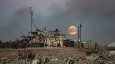 epa11779010 Displaced people walk near destroyed buildings as the full moon rises over Khan Yunis, southern Gaza Strip, 15 December 2024. According to the UN, at least 1.9 million people (or nine in ten people) across the Gaza Strip are internally displaced, including people who have been repeatedly displaced. EPA/HAITHAM IMAD