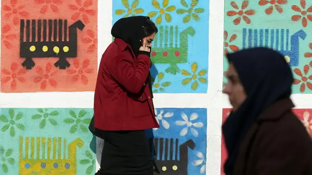 epa11790774 Iranian women walk past a mural on a street in Tehran, Iran, 23 December 2024.Â EPA/ABEDIN ATEHRKENAREH