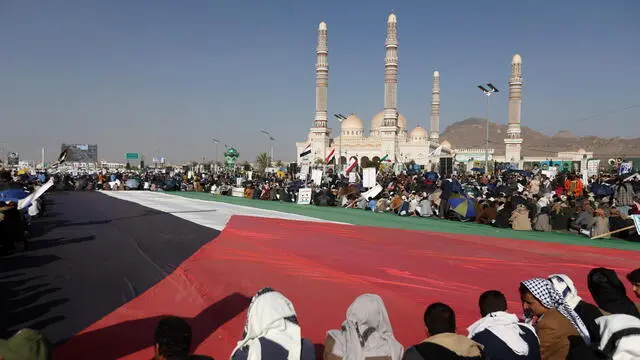 epa11787435 Houthi supporters gather around a large-scale Palestinian flag during an anti-US and anti-Israel protest in Sana'a, Yemen, 20 December 2024. Yemen's Houthis have attacked Israel with several drones, in a joint operation with Iranian-backed Iraqi militias, a day after Israel and the Houthis launched retaliatory strikes, Houthis' military spokesman Yahya Sarea said in a statement. EPA/YAHYA ARHAB