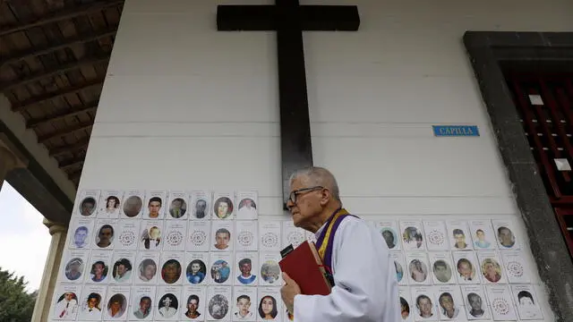 epa11199222 A priest walks in front of photographs of missing persons at the La Colina Pantheon cemetery in Rionegro, Colombia, on 04 March 2024. Intervention begins at the Rionegro cemetery, on the outskirts of Medellin, where the Unit for the Search for Disappeared Persons (UBPD) expects to recover thirty of the 152 unidentified bodies during the first phase. EPA/Luis Eduardo Noriega A.