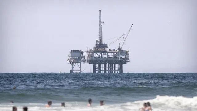 epa07874189 People swim in the Pacific Ocean next to the Huntington Beach Pier in front of an offshore oil rig in Huntington Beach, California, 02 August 2019. (issued 27 September 2019) With nearly 6,000 active oil and gas wells in the county, according to a Natural Resources Defense Council, Los Angeles remains the largest urban oil field in the US. Of the 18 million people leaving in greater Los Angeles, 600,000 live less than 400 meters from an active well. The story of the city is deeply intertwined with the oil industry. Old documents show Venice Beach covered with rigs and people walking the streets wearing gasmasks because the air pollution was so intense. This situation led to California being able to edict its own gas emission standards, stricter than those in the rest of the country, to counter the disastrous impact of the combined effects of oil production and traffic. This status was recently revoked by President Trump, a decision that is currently being challenged by the state of California. EPA/ETIENNE LAURENT