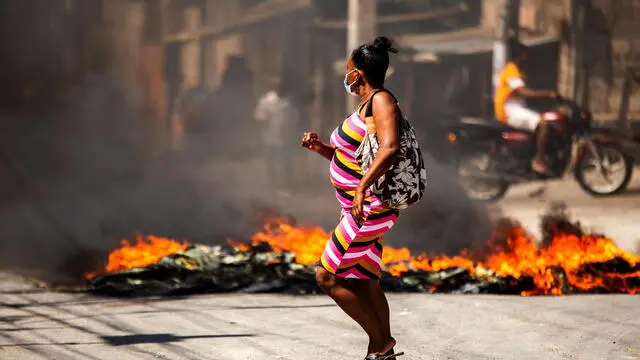 epa11555749 A woman walks past a fire barricade during a protest against gang violence in the Solino neighborhood of Port-au-Prince, Haiti, 19 August 2024. EPA/MENTOR DAVID LORENS