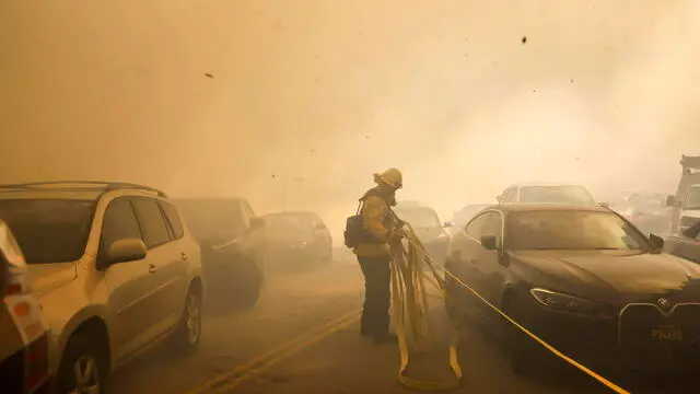 epaselect epa11811920 A Los Angeles firefighter drags a hose past cars trying to evacuate a neighborhood being threatened by the Palisades wildfire in Pacific Palisades, California, USA, 07 January 2025. According to the National Weather Service, large portions of the Los Angeles area are under extreme wildfire risk from 07 to 08 January due to high winds and dry conditions. EPA/CAROLINE BREHMAN