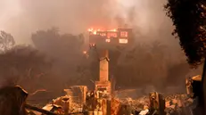 epa11813471 A house on fire and the remains of another burnt home in an area affected by the Palisades wildfire in Malibu, California, USA, 08 January 2025. According to data from California Department of Forestry and Fire Protection, CAL FIRE, the Palisades fire has burned through thousands of acres and has forced tens of thousands of evacuations in the Los Angeles area. EPA/ALLISON DINNER