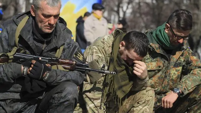 epa04656204 Volunteers of the 'Dnepr' battalion, one of them carrying his gun, kneel down as they pay tribute to a friend who was killed near the village of Shyrokino in the Donetsk region, during the funeral ceremony in Mariupol, Ukraine, 10 March 2015. US President Barack Obama and European Council President Donald Tusk on 09 March called for unity on Ukraine and discussed Europe's security challenges, including terrorism. Obama saluted German Chancellor Angela Merkel and French President Francois Hollande for their work in establishing the Minsk ceasefire process. EPA/IRINA GORBASYOVA