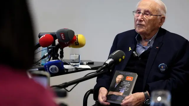 epa11838532 Holocaust survivor Albrecht Weinberg holds his book with the title 'That memories don't fade like the number on my arm, during an interview at the Memorial Place 'Former Jewish School' in Leer, Germany, 20 January 2025. Weinberg, one of the few remaining Holocaust survivors alive who can tell their stories, gives interviews to international journalists. EPA/FRIEDEMANN VOGEL