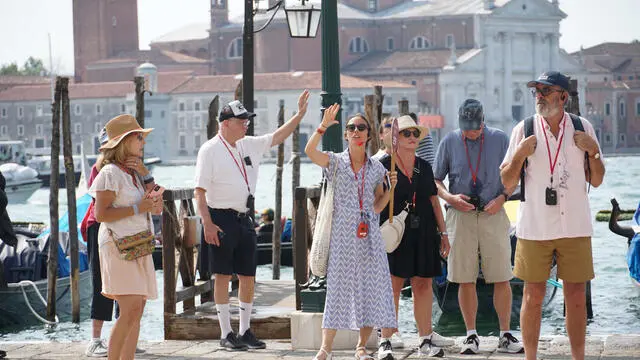 Una guida turistica accompagna un gruppo di visitatori verso piazza San Marco, usando un radio microfono per comunicare con loro, Venezia 1 agosto 2024: a partire da oggi l’amministrazione comunale applica l’ordinanza che impone la riduzione delle dimensioni delle comitive in visita nel centro storico e vieta l’uso di altoparlanti alle guide accompagnatrici. ANSA/ANDREA MEROLA