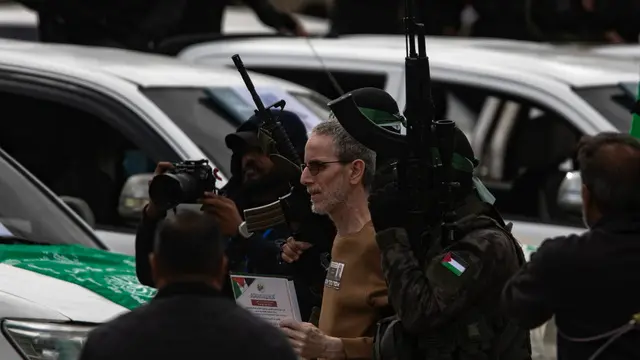 epa11882144 Palestinian fighters from Hamas's Izz ad-Din al-Qassam Brigades escort Israeli hostages Ohad Ben-Ami (pictured), Or Levi and Eli Sharabi onto the stage before handing them over to a Red Cross team in Deir al-Balah, central Gaza, 08 February 2025. In exchange, Israel will release 183 Palestinian prisoners and detainees. EPA/HAITHAM IMAD