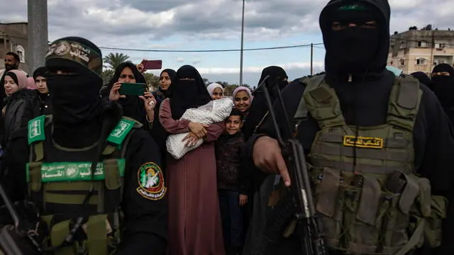 epa11882413 Palestinians with Izz ad-Din al-Qassam fighters after the handing over of three Israeli hostages to the Red Cross as part of a Gaza ceasefire agreement with Israel in Deir al-Balah, central Gaza Strip, 8 February, 2025. In exchange, Israel will release 183 Palestinian prisoners and detainees. EPA/HAITHAM IMAD