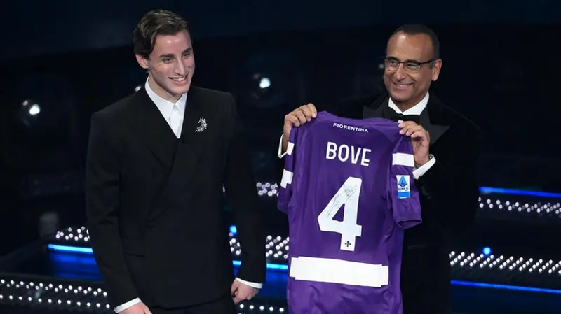 Italian soccer player Edoardo Bove (L) and Sanremo Festival host and artistic director Carlo Conti holds the Fiorentina football team jersey on stage at the Ariston theatre during the 75th edition of the Sanremo Italian Song Festival, in Sanremo, Italy, 15 February 2025. The music festival will run from 11 to 15 February 2025. ANSA/ETTORE FERRARI