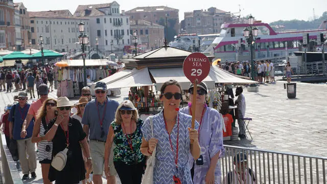 Una guida turistica accompagna un gruppo di visitatori verso piazza San Marco, usando un radio microfono per comunicare con loro, Venezia 1 agosto 2024: a partire da oggi l’amministrazione comunale applica l’ordinanza che impone la riduzione delle dimensioni delle comitive in visita nel centro storico e vieta l’uso di altoparlanti alle guide accompagnatrici. ANSA/ANDREA MEROLA