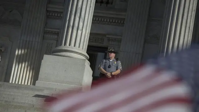 epa04811736 A Police Officer stands guard during a rally calling for the Confederate flag to be taken down, at the South Carolina State House Building in Columbia, South Carolina, USA, 20 June 2015. Debate about the Confederate flag from the US Civil War that still flies on South Carolina's State House grounds in Columbia has flared since the racially motivated shooting in Charleston on 17 June, in which 9 people were murdered. 21 year-old suspect Dylann Storm Roof was arrested in North Carolina on 18 June. Calls for taking down the flag have grown on social media after the flag was seen flying at full staff, while the South Carolina and US flags flew at half staff in honour of the victims. EPA/JOHN TAGGART