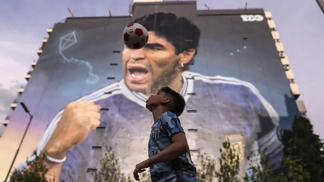 epa10273261 Children play soccer near a mural in honor of Diego Armando Maradona made by Martin Ron, in Buenos Aires, Argentina, 28 October 2022 (issued 29 October 2022). The death of Diego Armando Maradona led to countless tributes throughout Argentina. His figure appears on altars, popular shrines and street paintings, and now by two hyper-realistic murals by Argentinian visual artist Martin Ron. EPA/Juan Ignacio Roncoroni