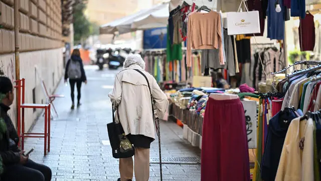 Una donna anziana cammina tra le bancarelle nel quartiere Prati di Roma, 31 ottobre 2024. ANSA/ALESSANDRO DI MEO (generica, simbolica, anziana, anziani, mercato, passeggio, shopping, bastone, autunno, inverno, vestiti, bancarelle)