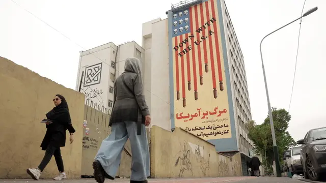 epaselect epa12026543 People walk next to an anti-US mural in a street in Tehran, Iran, 12 April 2025. Top Iranian and US officials will hold indirect negotiations in Oman on 12 April amid the ongoing tensions between the USA, Israel and Iran. EPA/ABEDIN TAHERKENAREH EPA-EFE/ABEDIN TAHERKENAREH