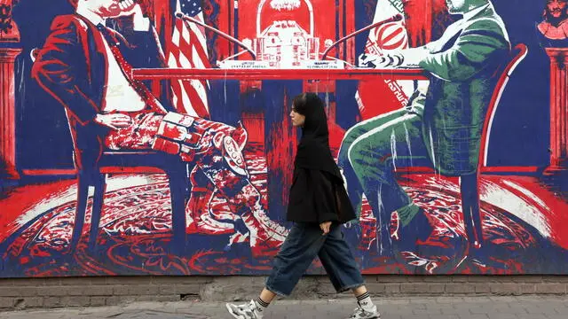 epa12026536 A woman walks near an anti-US mural depicting a negotiation table next to the former US embassy in Tehran, Iran, 12 April 2025. Top Iranian and US officials will hold indirect negotiations in Oman on 12 April amid the ongoing tensions between the USA, Israel and Iran. EPA/ABEDIN TAHERKENAREH