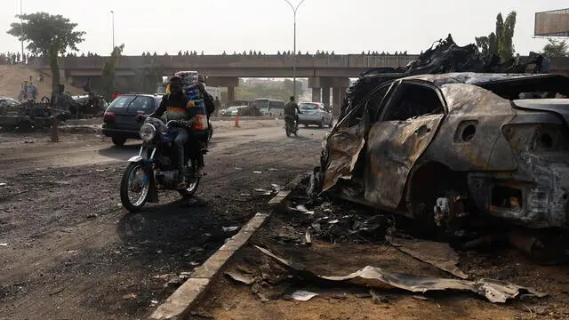 epaselect epa11975522 Motorcyclists ride past the wreckage of vehicles burned during the explosion of a Compressed Natural Gas (CNG) truck near Karu Bridge in Abuja, Nigeria, 20 March 2025. The Federal Capital Territory Emergency Management Department said that the accident occurred when the CNG truck driver lost control and collided with other vehicles on 19 March, leading to the explosion and the destruction of dozens of other vehicles. EPA/AFOLABI SOTUNDE