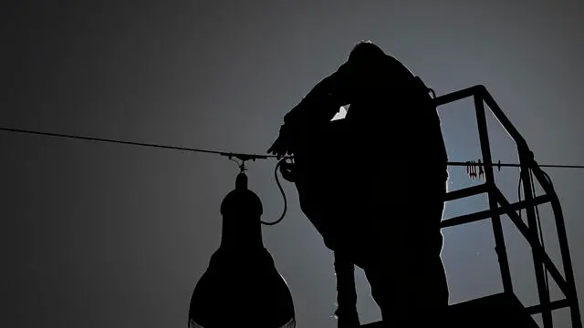 Un uomo impegnato nella manutenzione di un lampione stradale a Napoli, 25 novembre 2024. ANSA/CIRO FUSCO (simbolica, generica, uomo, controluce, silhouette, lavoratore, gru, scala)
