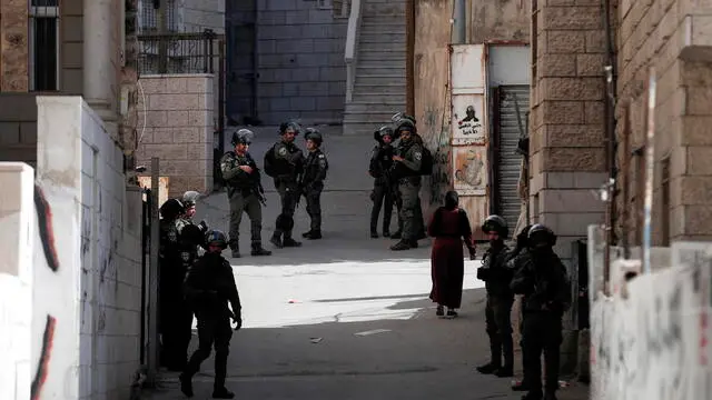 epa10428753 A Palestinian woman passes next to Israeli police on guard during the demolishing of a Palestinian house at Shuafat refugee camp in east Jerusalem belonging to the family of Udai Tamimi, 25 January 2023. According to Israeli Police on 19 October 2022, Udai Tamimi, who was wanted in connection with an attack at a refugee camp on 08 October 2022, was shot in an exchange of gunfire with guards after a second attack attempt at a checkpoint near Jerusalem. EPA/ATEF SAFADI