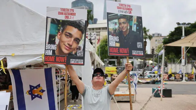 epa12093343 A man holds photos depicting Israeli-American soldier Edan Alexander, currently held captive in the Gaza Strip, as people gather to watch a live stream of his release, outside the Kirya military base in Tel Aviv, Israel, 12 May 2025. According to Israeli defence forces some 58 hostages remain captive inside the Strip since 07 October 2023. EPA/ABIR SULTAN