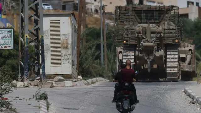 epa12122817 Palestinians ride a motorbike past bulldozers deployed during an Israeli military operation in the West Bank city of Jenin, 21 May 2025. The Israeli military has been conducting a four-month operation in Jenin and its camp since 21 January. EPA/ALAA BADARNEH