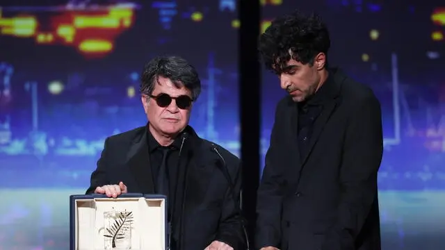 epa12132926 Iranian director and screenwriter and producer Jafar Panahi (L)speaks on stage after winning the Palme d'Or for the film "Un simple accident" (A Simple Accident) during the closing and awards ceremony of the 78th annual Cannes Film Festival, in Cannes, France, 24 May 2025. The film festival runs from 13 to 24 May 2025. EPA/MOHAMMED BADRA