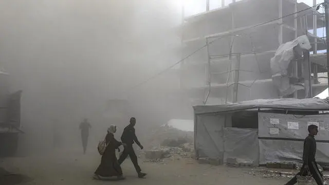 epa12127724 Palestinians walk amidst smoke engulfing a road following an Israeli airstrike west of Gaza City, in Gaza Strip, 23 May 2025. More than 53,700 Palestinians have been killed in the Gaza Strip, according to the Palestinian Ministry of Health, since Israel launched a military campaign in the strip in response to a cross-border attack led by the Palestinian militant group Hamas on 07 October 2023, in which about 1,200 Israelis were killed and more than 250 taken hostage. EPA/MOHAMMED SABER