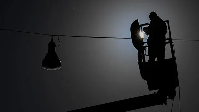 Un uomo impegnato nella manutenzione di un lampione stradale a Napoli, 25 novembre 2024. ANSA/CIRO FUSCO (simbolica, generica, uomo, controluce, silhouette, lavoratore, gru, scala)