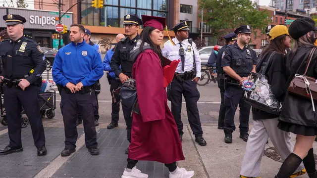 epa12129172 A graduate walks past police officers monitoring students, graduates, faculty, and others (unseen) supporting Palestine in a protest against the City University of New York and Barclays’ involvement with Israel outside the Barclays Center during the Brooklyn College commencement ceremony in Brooklyn, New York, USA, 23 May 2025. EPA/SARAH YENESEL