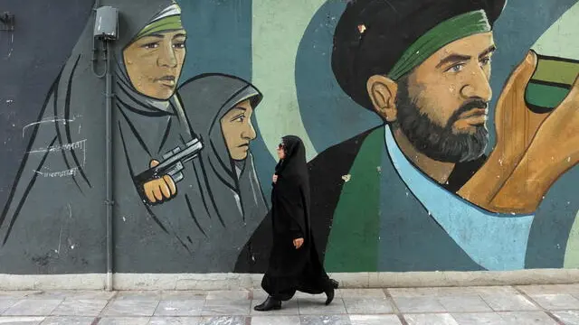 epa12074426 A veiled Iranian woman walks next to a wall painting of Iran's revolutionary guards soldiers in a street in in Tehran, Iran, 05 May 2025. A fourth round of US-Iran nuclear talks, which was scheduled to be held in Rome on 03 May 2025, has been postponed amid continued tensions. EPA/ABEDIN TAHERKENAREH