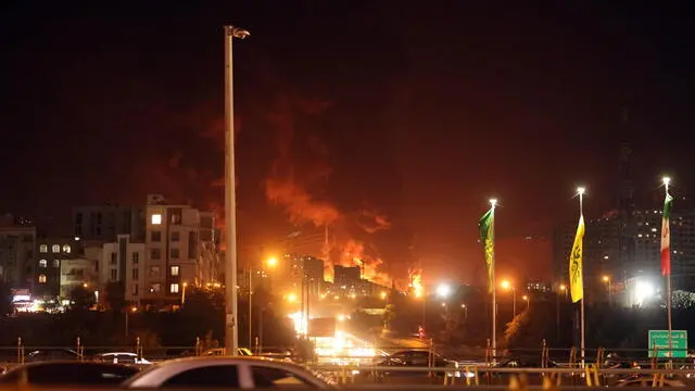 epa12175988 People drive as fire and smoke rise from an oil warehouse in Tehran, Iran, 15 June 2024. Israel continues its strikes on Iran's nuclear program and energy facilities. EPA/ABEDIN TAHERKENAREH