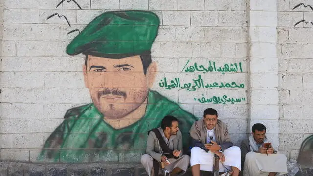 epa12175721 Houthi supporters sit beneath graffiti depicting a portrait of a war-slain Houthi fighter, during a ceremony marking the Shiite religious Day of Eid al-Ghadir, in Sana'a, Yemen, 14 June 2025. The al-Ghadir Day is annually observed since Shiites believe the Prophet Muhammad designated his cousin Imam Ali as his successor. Yemen's Shiite Houthis have celebrated al-Ghadir Day since they took control of most northern parts of Sunni majority-Yemen, including the capital Sana'a, in 2014. EPA/YAHYA ARHAB