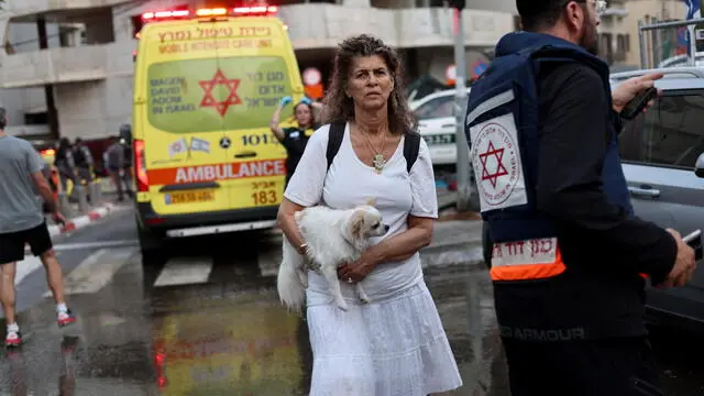 epa12178326 A woman (C) carries a dog as Israeli rescue teams and medical personnel gather at the scene where Iranian ballistic missiles struck buildings in Tel Aviv, Israel, 16 June 2025. According to emergency service, Magen David Adom (MDA), paramedics have pronounced the death of four people and provided medical care to a total of 81 injured, one in serious condition and five in moderate condition. EPA/ATEF SAFADI