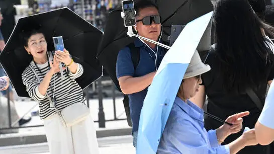 Turisti camminano utilizzando ombrelli per proteggresi dal sole mentre fotografano con i loro smartphone la fontana diPiazza Castello, Milano, 13 giugno 2025. ANSA/DANIEL DAL ZENNARO