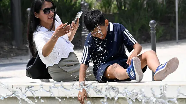Turistii cercano refrigerio dal caldo nella fontana di Piazza Castello, Milano, 13 giugno 2025. ANSA/DANIEL DAL ZENNARO