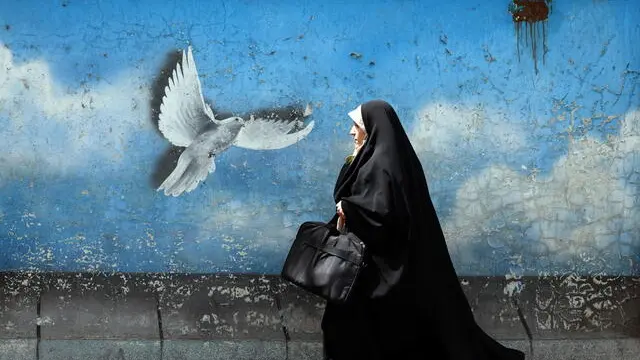 epa12017447 A veiled Iranian woman walks next to peace bird wall painting in a street, in Tehran, Iran, 08 April 2025. Iranian Foreign Minister Abbas Araqchi said on 08 April that top Iranian and US officials will hold indirect negotiations in Oman on 12 April. EPA/ABEDIN TAHERKENAREH