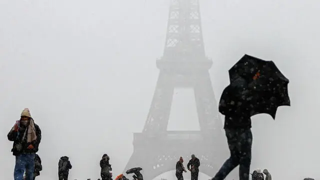 epaselect epa11733276 People with their umbrellas walk during snowfall near the Eiffel Tower in Paris, France, 21 November 2024. French National Weather and Climate Service Meteo-France issued an 'orange' warning in 32 departments from northern Brittany and Normandy to the Ile-de-France due to snowfall and freezing rain forecasted on 21 November. EPA/MOHAMMED BADRA